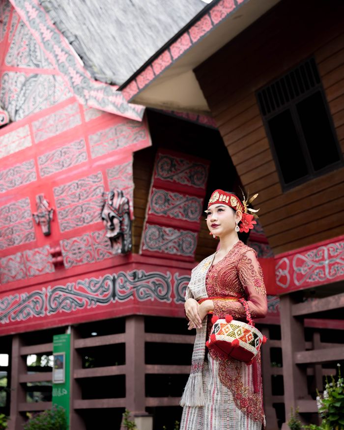 Woman in traditional Indonesian dress poses by ornate traditional building.